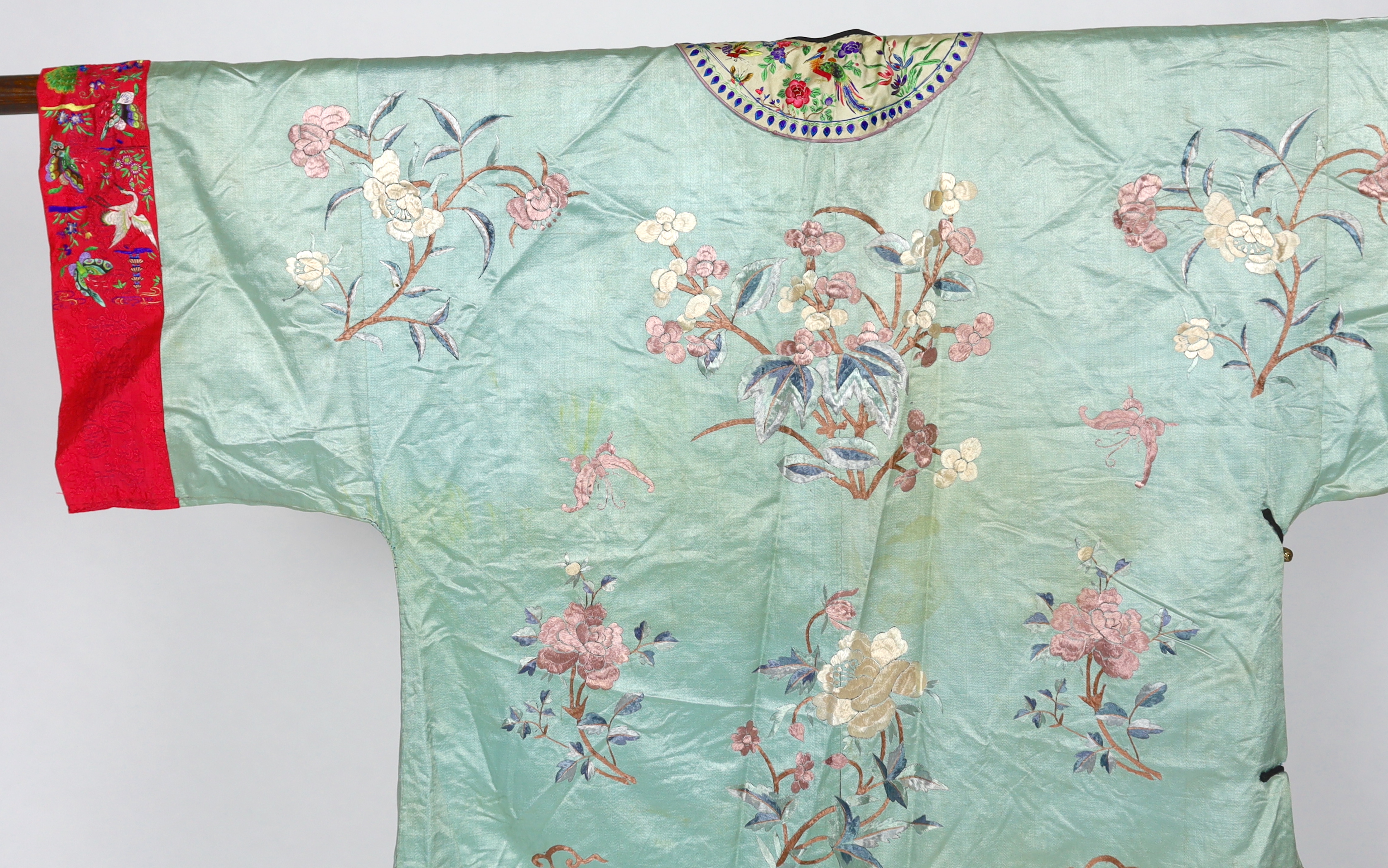 An early 20th century Chinese silk embroidered turquoise robe, embroidered in pastel silk with butterflies and flowers all over, polychrome embroidered braiding edged with lilac and bright pink sleeve bands embroidered w